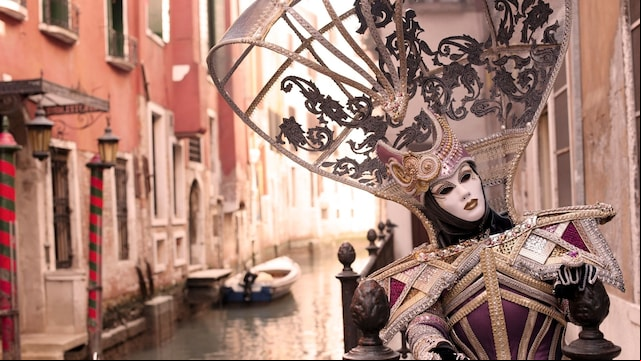 Mujer con disfraz medieval típico de los Carnavales de Venecia en un canal de la ciudad.