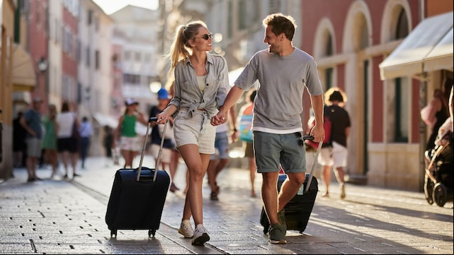 Pareja feliz por las calles empedradas de una ciudad con ropa de primavera, paseando con su maleta de cabina