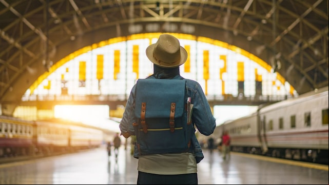 Joven con una mochila de viaje a su espalda en el centro del andén de una estación de tren
