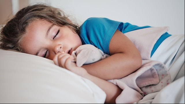 Niña duermiendo abrazada a su 'doudou' muy plácidamente en la cama en primer plano