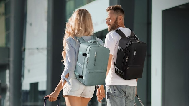 Una pareja con su mochila de viaje y sus maletas de cabina caminando de la mano en un aeropuerto con 'outfit' de verano